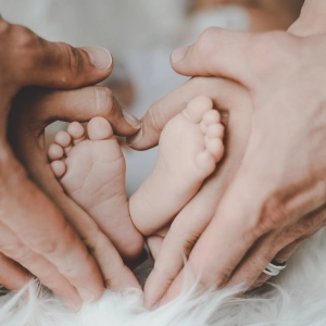 Image of a couple holding their infant's feet, forming a heart sign